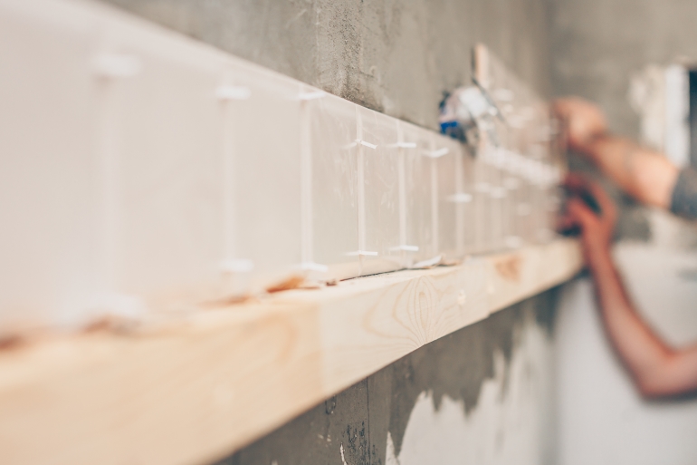 The tiler puts the first row of tiles on the kitchen wall at the laser level by By VanoVasaio on Shutterstock